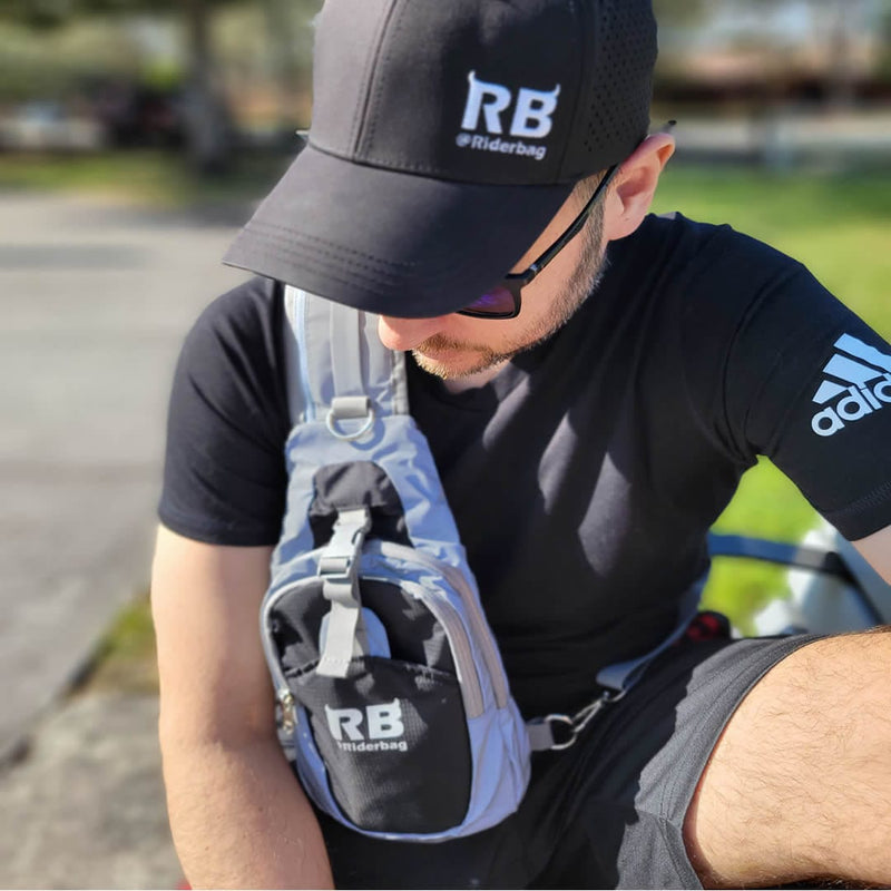 Load image into Gallery viewer, Man seated on his bike opening the Riderbag sling bag worn across his chest for hands-free access