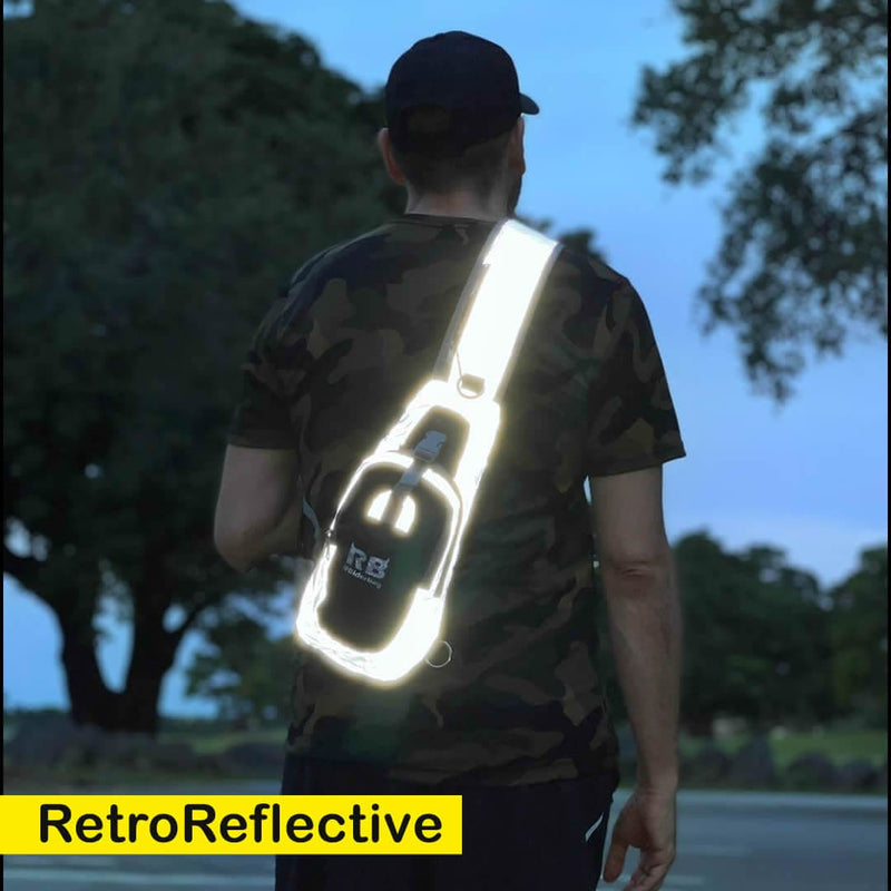 Load image into Gallery viewer, Man walking outdoors at dusk wearing the Riderbag sling bag across his back, the retro-reflective strap glowing white