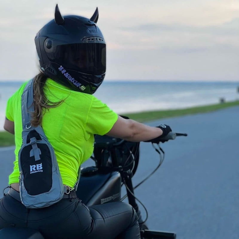 Load image into Gallery viewer, Woman on a motorcycle by the ocean, seen from behind, wearing the Riderbag reflective sling bag over a hi-vis shirt